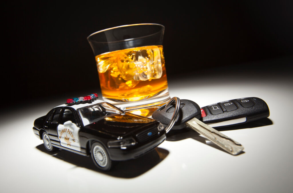 Highway Patrol Police Car Next to Alcoholic Drink and Keys Under Spot Light. This is a picture for a blog about needing to hire a trial lawyer.